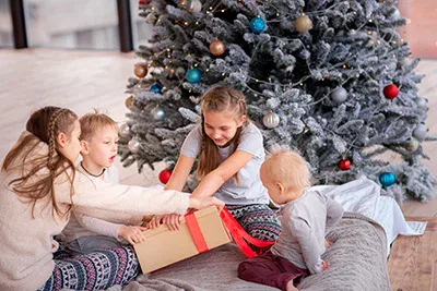 Eine Gruppe Kinder spielt mit einem Weihnachtsgeschenk vor einem Weihnachtsbaum.