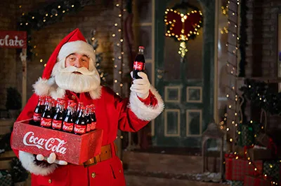 Ein Weihnachtsmann hält eine Schachtel Coca-Cola.